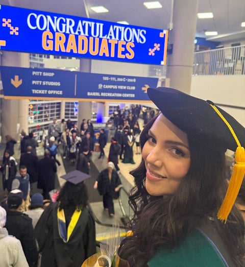 A woman in graduation regalia smiles at the camear