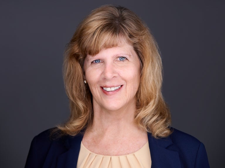 Woman with auburn blonde hair wearing a black cardigan over a tan blouse.