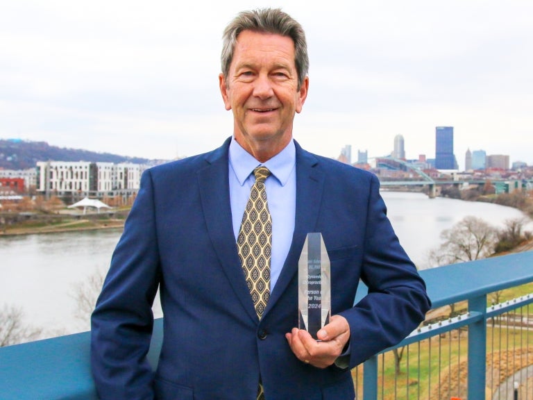 Michael Schneider holding his award in his left hand and smiling with the Pittsburgh skyline in the background