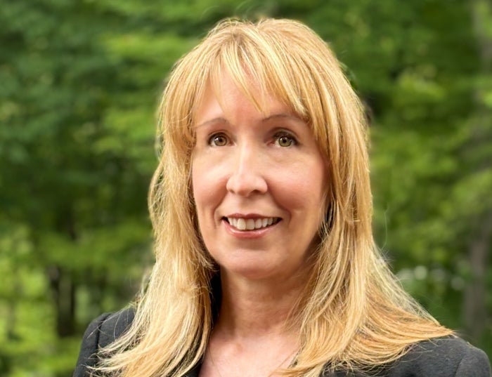 Woman with blonde hair wearing a black shirt in front of a green outdoor background.