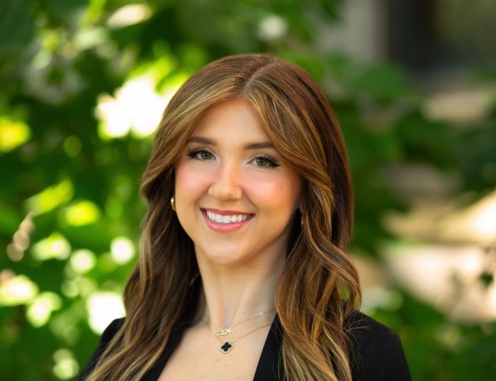 Woman with brown hair wearing a black shirt in front of greenery.