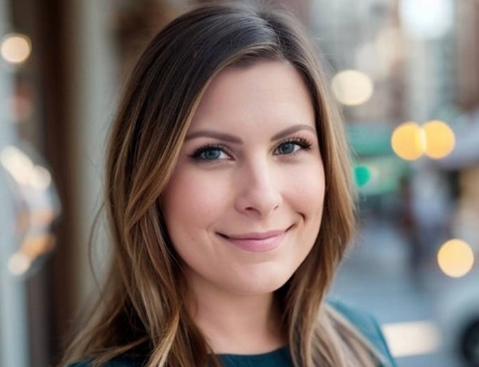 Woman with brown hair in a dark green sweater with lights in the background.