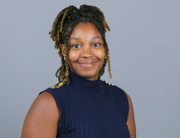 Woman with dark brown hair in a navy blue shirt in front of a gray background.