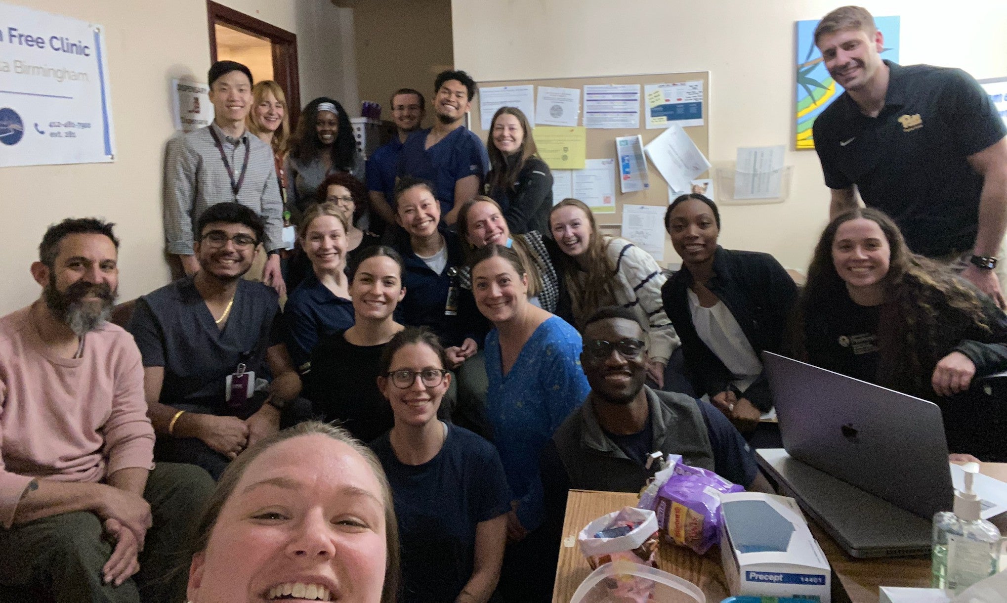 A room at the Birmingham Free Clinic is full of smiling people standing and sitting 