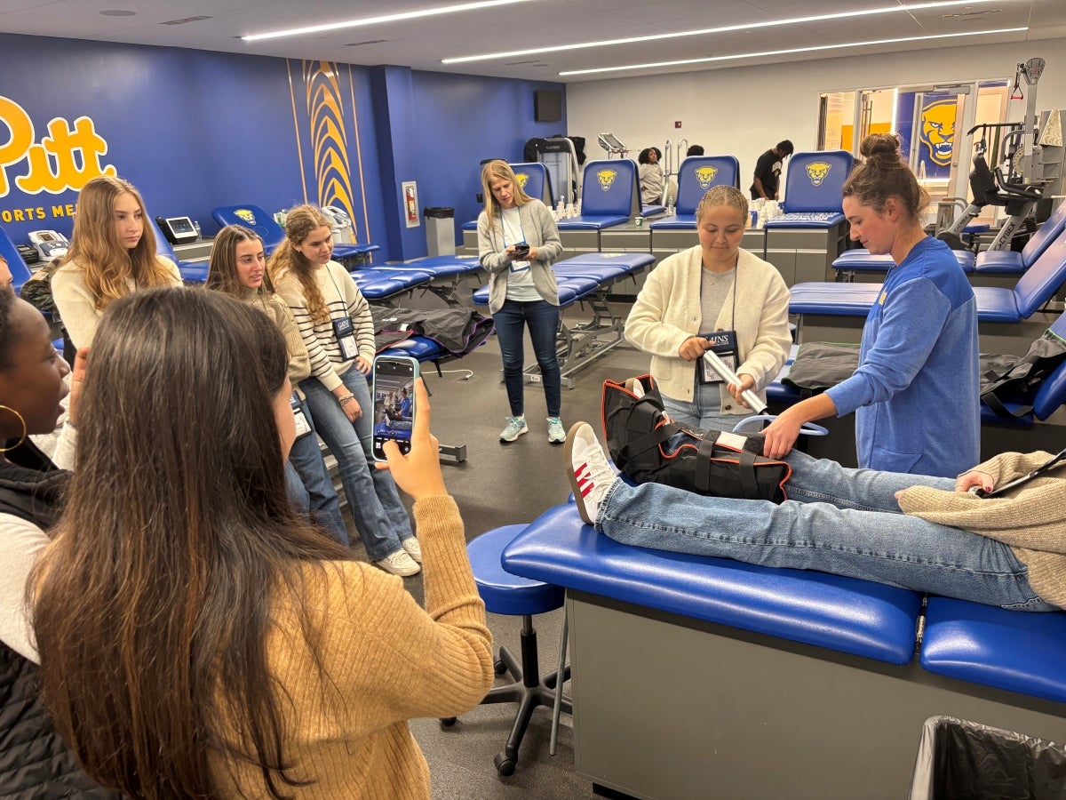 An instructor demonstrates splinting a leg to a group of young women