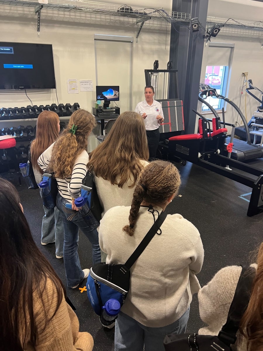 A group of young women listen to an instructor in front of testing equipment