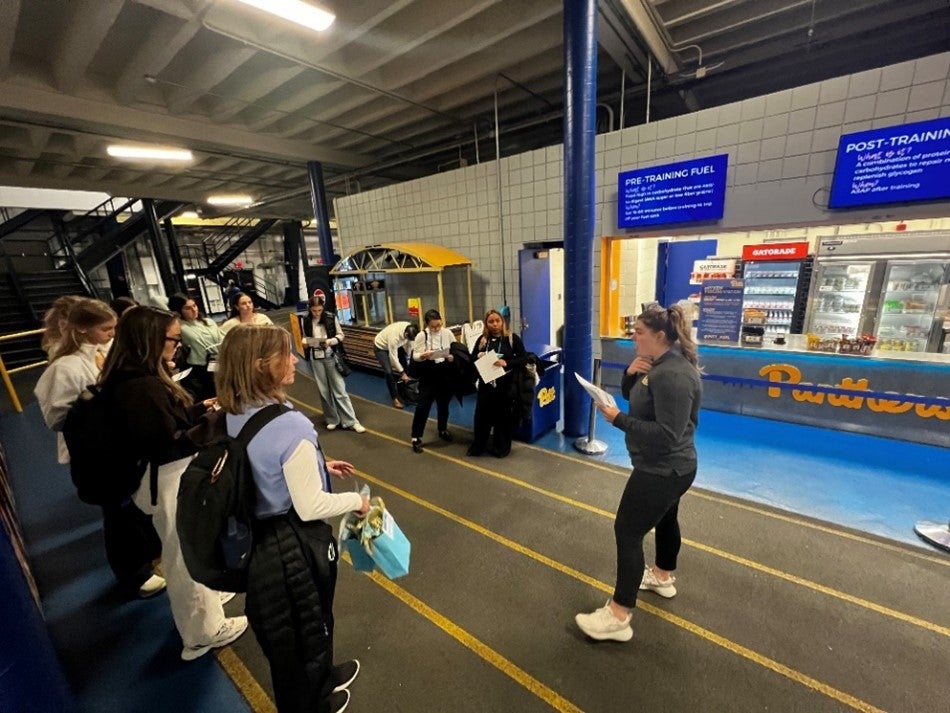 A group of women listen to a lecture on an indoor running track