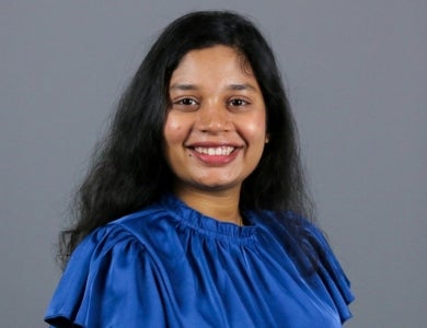 Woman with long black hair wearing a dark blue ruffled blouse.