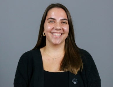 Woman with brown hair wearing a black cardigan in front of a gray background.