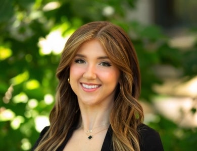 Woman with brown hair wearing a black shirt in front of greenery.