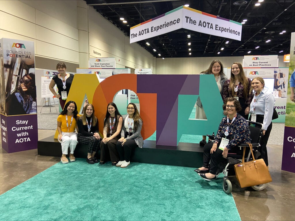 Women sitting in front of a cut out of the letters AOTA.