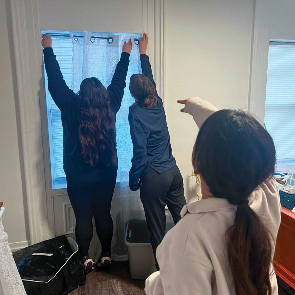 Three students working together to hang curtains in a bedroom.