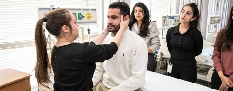 Student with ponytail assessing another student by placing their hands on their head.