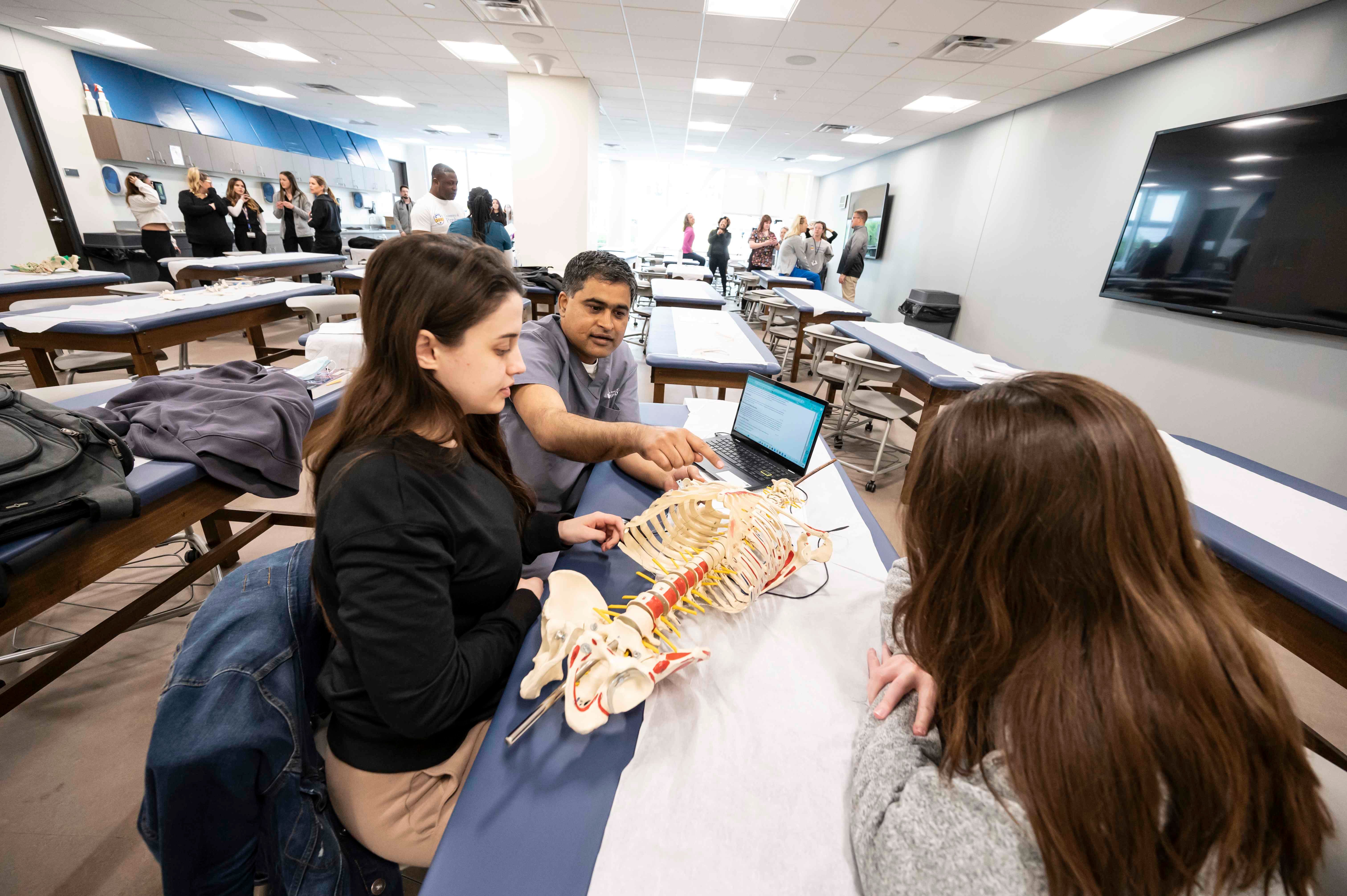 Three students working around a skeletal torso model.