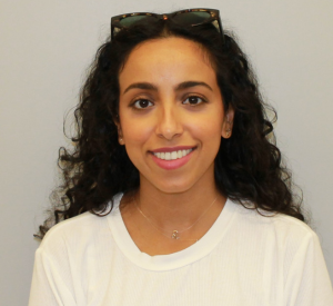 Woman with brown curly hair wearing sunglasses and a white top.