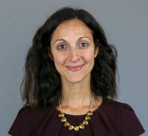 Woman with brown hair wearing a brown blouse and a gold necklace.