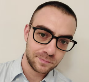 Man with short brown hair wearing black glasses wearing a light gray collared shirt.