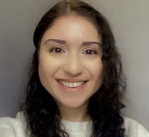 Woman with dark curly hair wearing a white sweater.