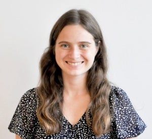 Woman with long brown hair wearing a black blouse with white polka dots on it.