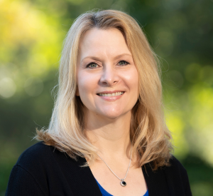 Woman with blonde hair wearing a black cardigan over a blue shirt.