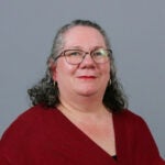 Woman with short dark gray curly hair wearing a red sweater.