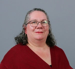 Woman with short dark gray curly hair wearing a red sweater.