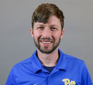 Man with short brown hair and a beard wearing a blue Pitt polo with the yellow Pitt script.