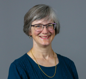 Woman with short gray hair wearing black and silver glasses and a navy blue sweater.