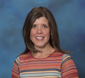 Woman with brown hair wearing a red, blue and yellow striped shirt.