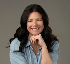 Woman with long, dark brown hair wearing a light blue denim button up shirt.