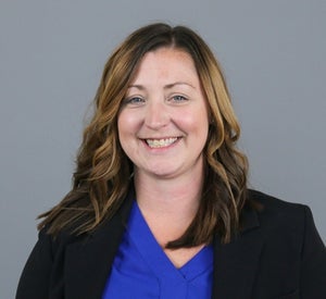 Woman with brown hair and highlights wearing a black blazer and a bright blue blouse.