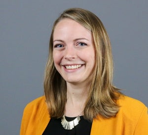 Woman with dark blonde hair wearing a bright orange blazer over a black top and a gold necklace.