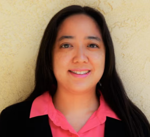 Woman with long dark hair wearing a black cardigan over a bright pink collared shirt.