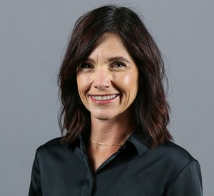 Woman with short brown hair wearing a black blouse and a gold necklace.