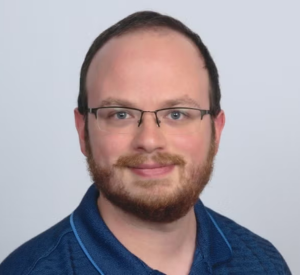 Man with short auburn hair wearing a dark blue collared shirt.