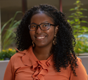 Woman with dark curly hair wearing a peach colored blouse and gold earrings.