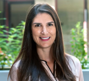 Woman with dark brown hair wearing a tan shirt with black detailing.