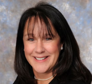 Woman with dark hair wearing a black blacker and a pearl necklace.