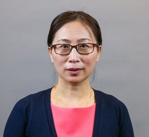 Woman with black hair pulled back wearing a navy blue sweater over a pink blouse.