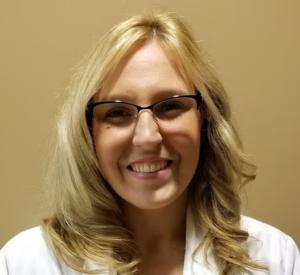 A woman with blonde curled hair wearing a white cardigan.