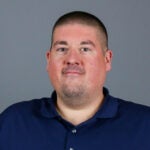 Man with short black hair wearing a navy blue shirt.