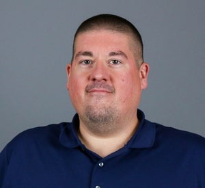 Man with short black hair wearing a navy blue shirt.