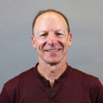 Man with short brown hair wearing a maroon shirt.