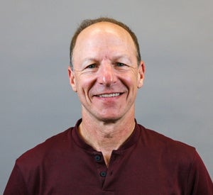 Man with short brown hair wearing a maroon shirt.