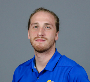 Man with short red hair wearing a blue collared shirt.