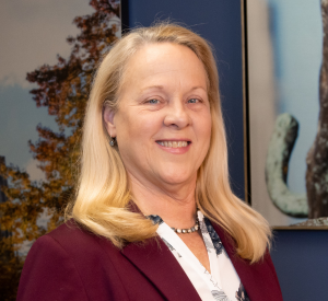 Woman with blonde hair wearing a dark red blazer over a black and white floral blouse.