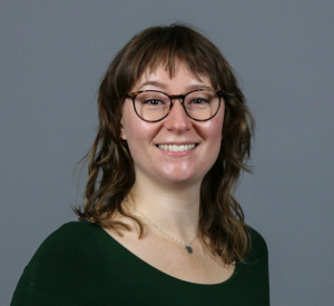 Person with brown hair wearing tortoise shell glasses and a black shirt.