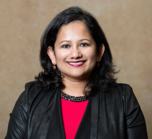 A woman with black hair wearing a black jacket over a red top and a black beaded necklace.