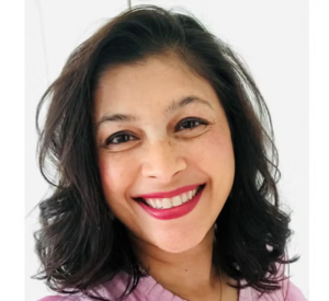 A woman with brown curly hair wearing a pink blouse.