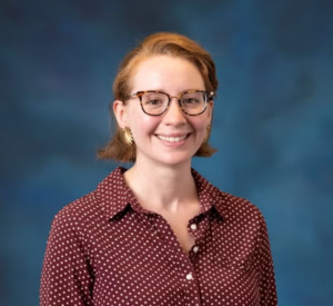 Woman with red hair wearing a brown collared blouse.